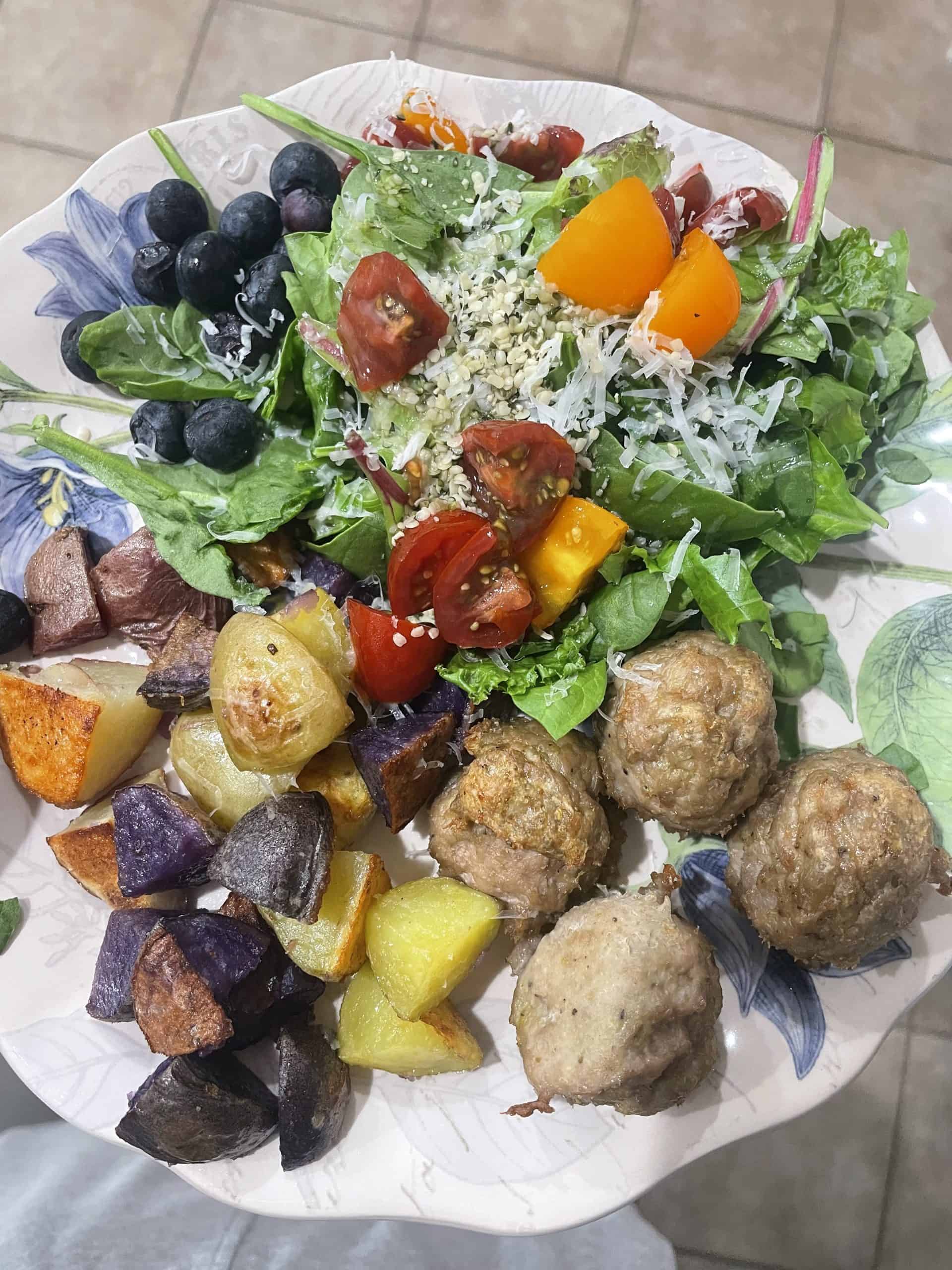 turkey meatballs next to roasted potatoes and a salad with sliced tomatoes on top