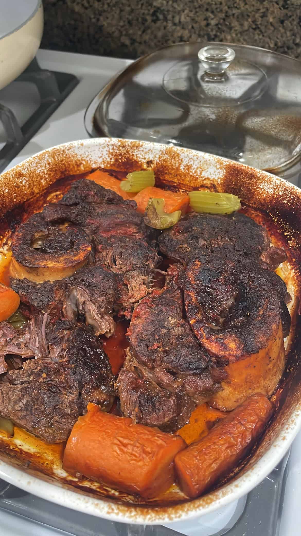 baked beef shank with roasted carrots and celery sitting on a stove top