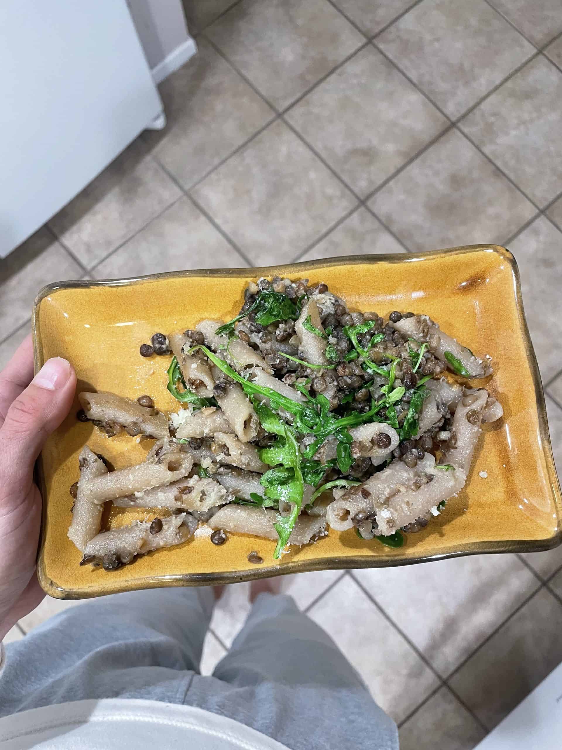 gluten free pasta with lentils and arugula on top of a square mustard colored plate