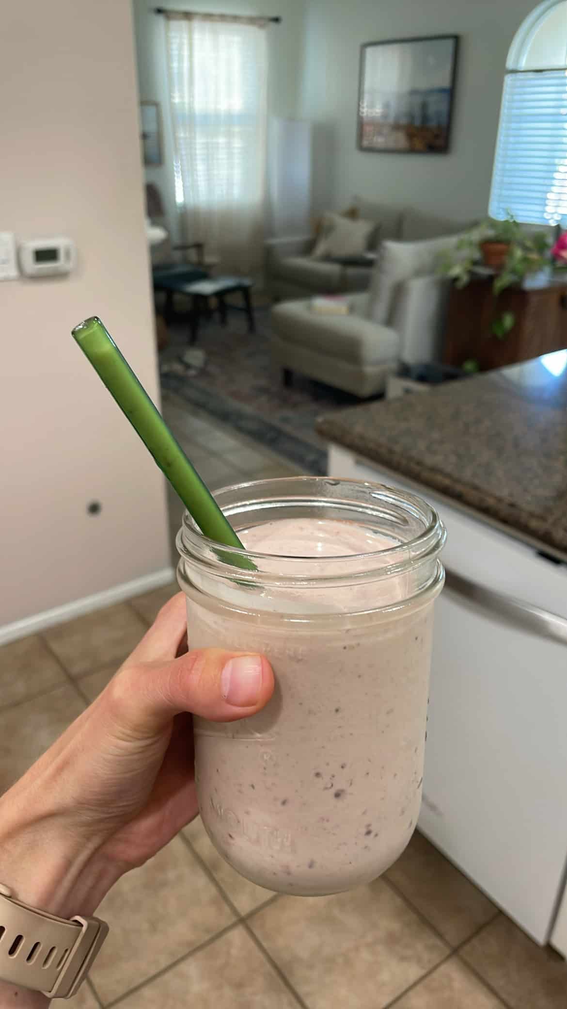pink protein smoothie in a glass jar with a green glass straw