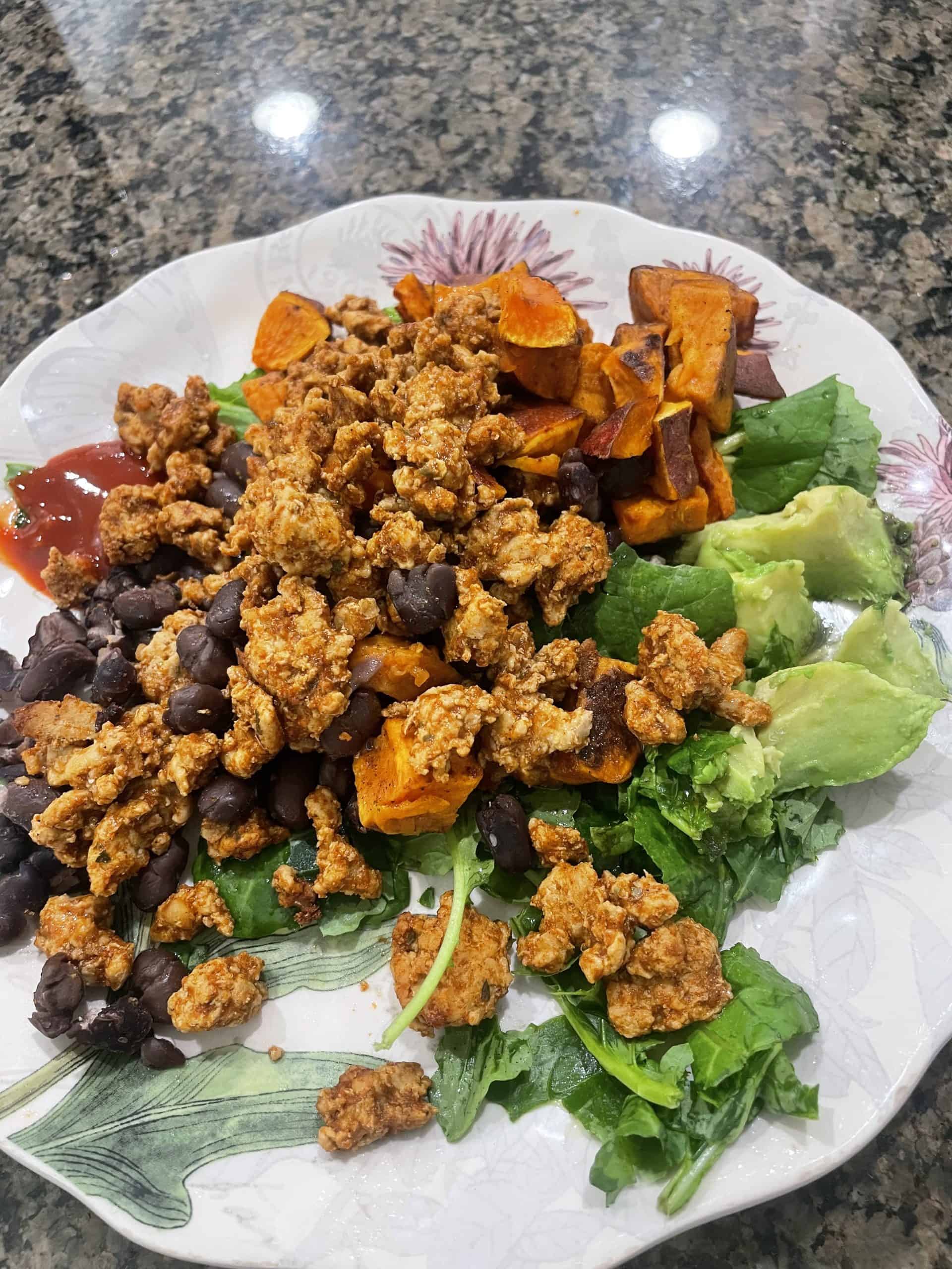 taco meat on top of black beans with sweet potatoes, avocado on a bed of dark leafy greens