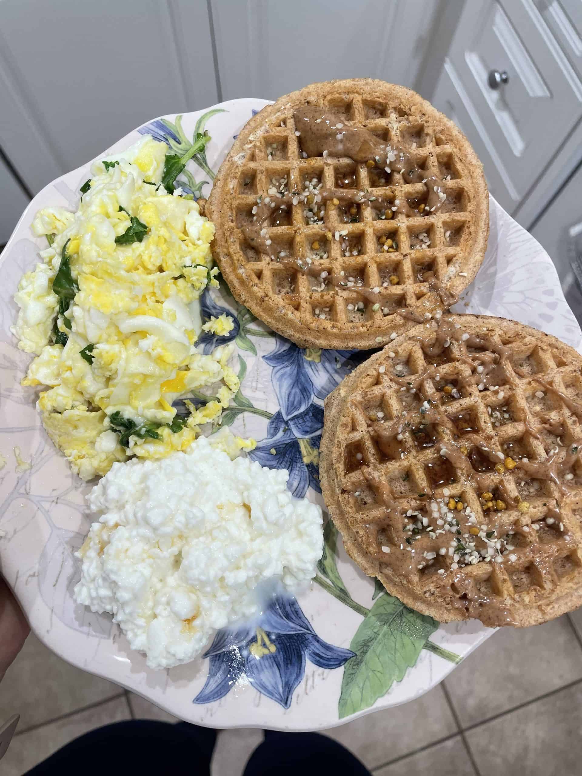 scrambled eggs with spinach, cottage cheese and two whole wheat waffles on the side with maple syrup, almond butter and hemp seeds on top