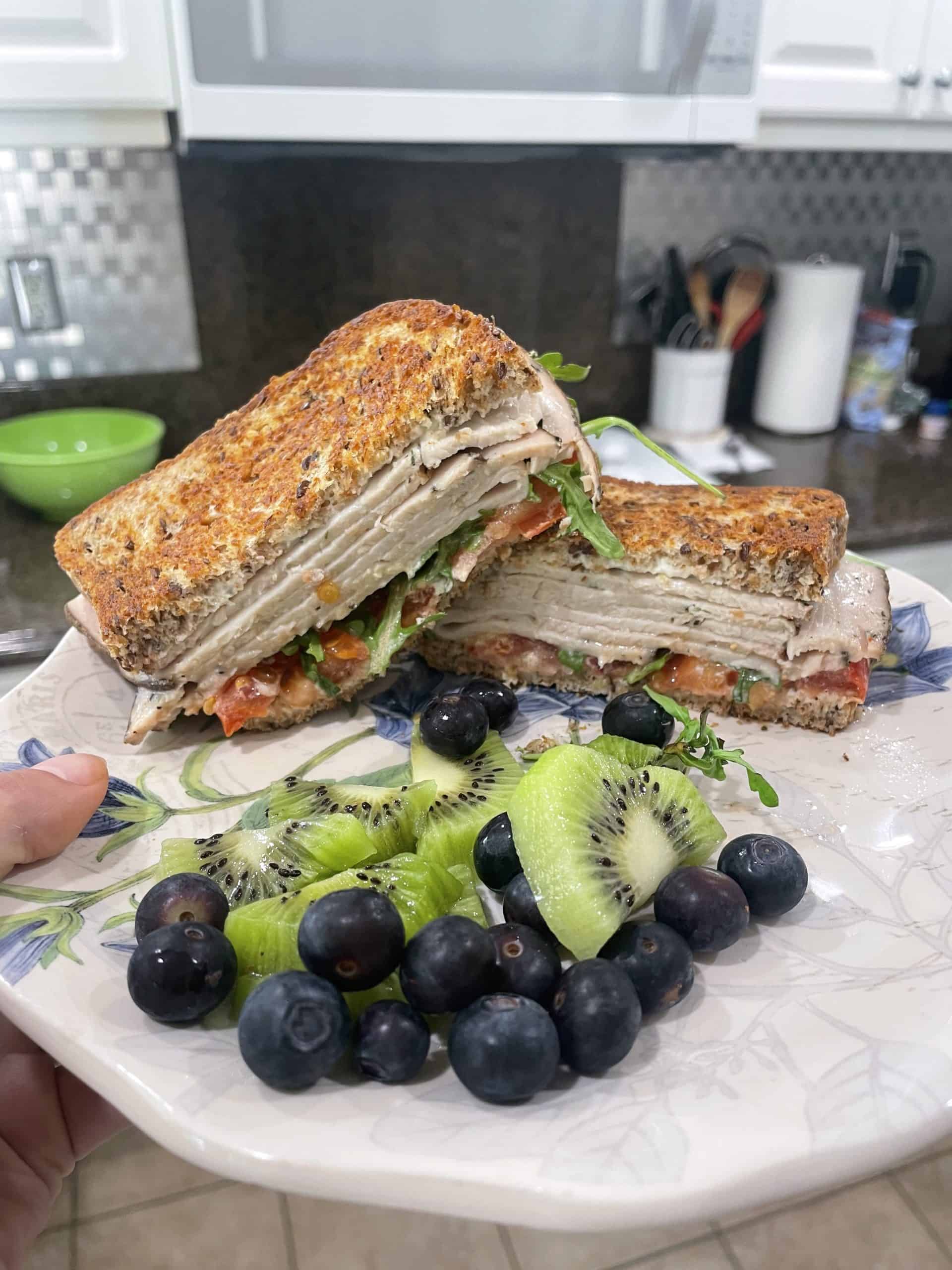 turkey sad which with leafy greens, tomato on whole wheat bread and sliced kiwi and blueberries on the side