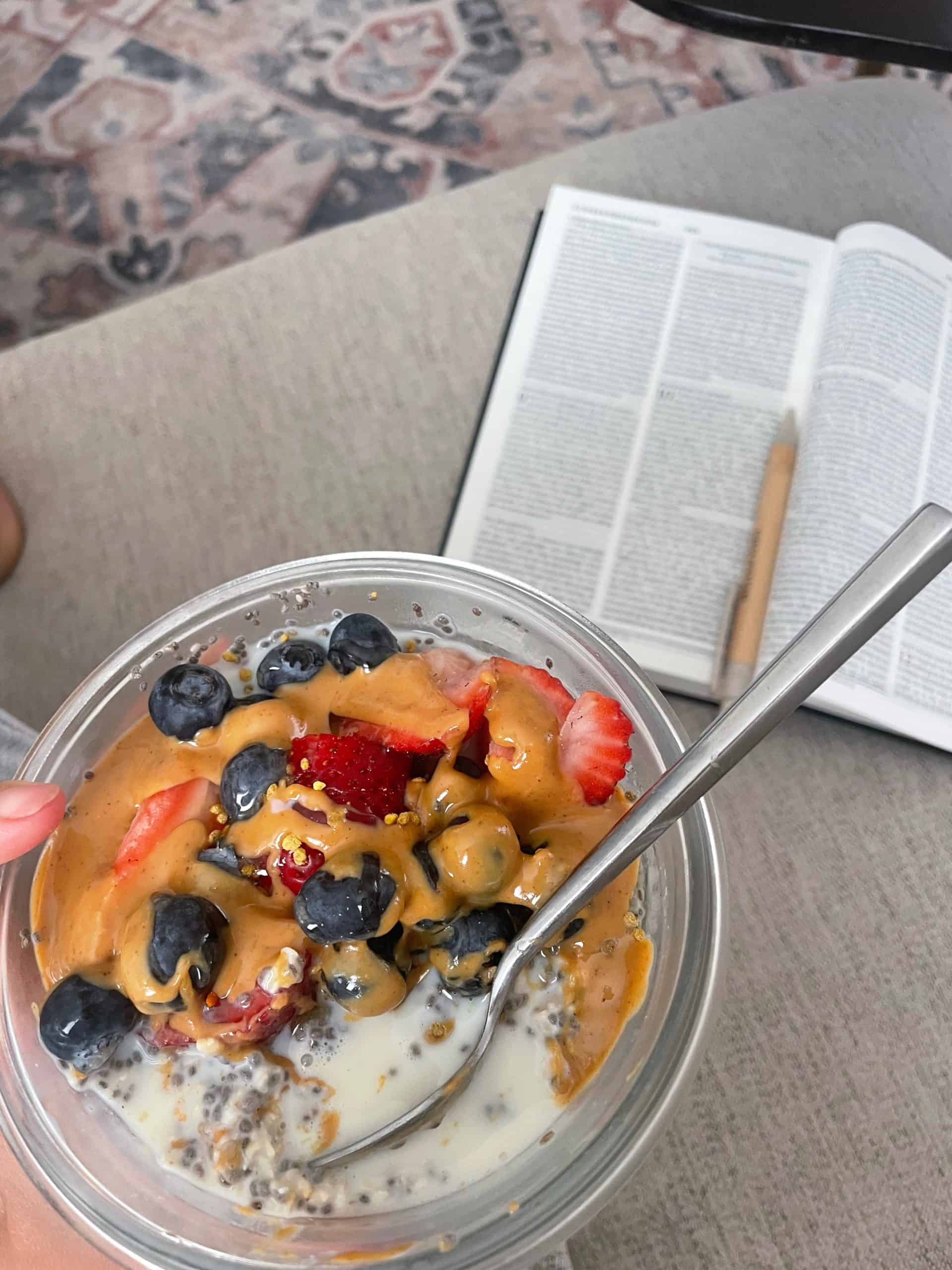 bowl of overnight oats with blueberries, strawberries and peanut butter and a bible in the background