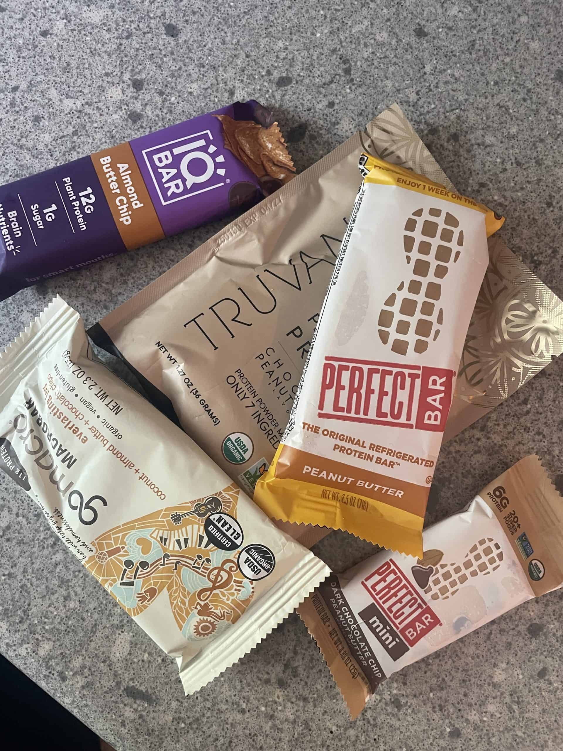 protein bars thrown on a counter top including things like IQ bar, go macro bar, perfect bar and a truvani protein powder packet