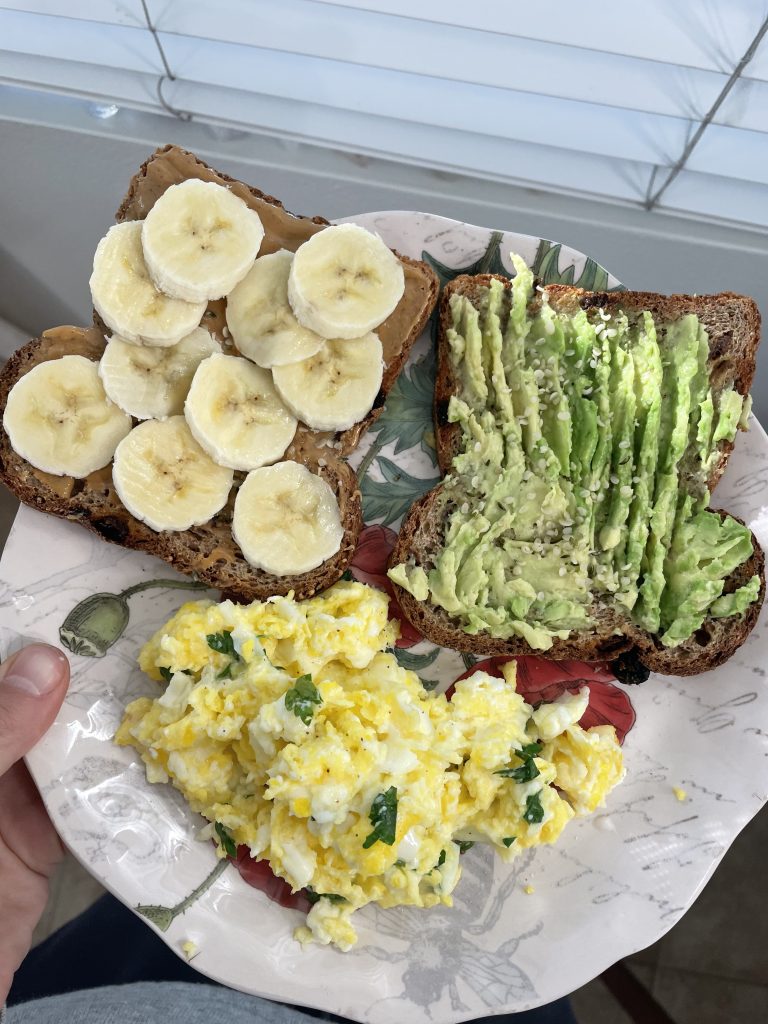 plate with scrambled eggs, and two pieces of toast with avocado on one and bananas on the other