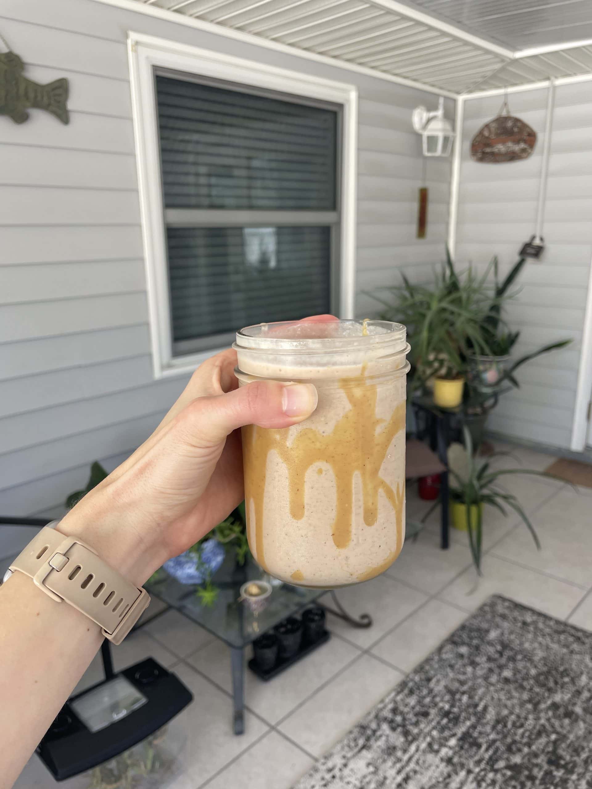 a hand holding a mason jar with a brown smoothie inside