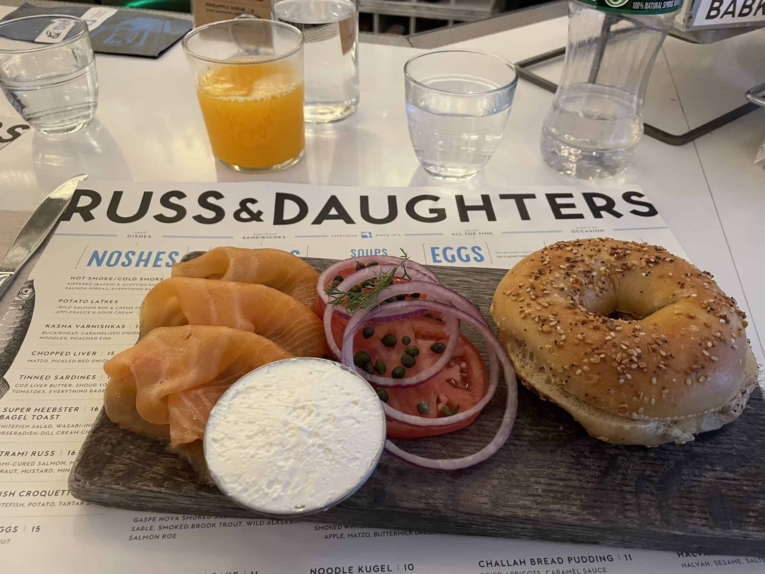 russ & daughters placemat with a lox bagel on top of it with onion, cream cheese and capers on the side