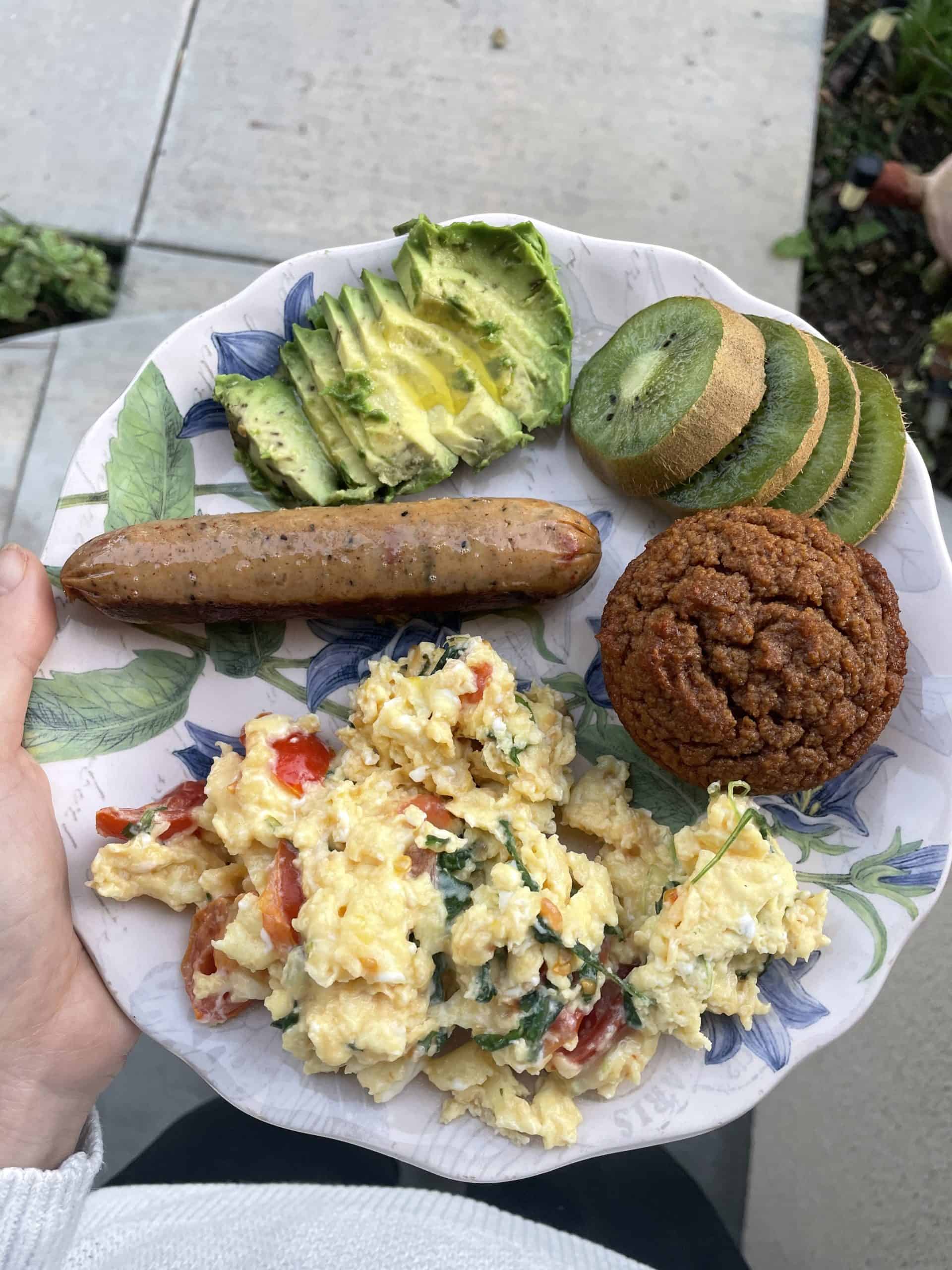 plate of food with scrambled eggs, kiwi, avocado and a muffin