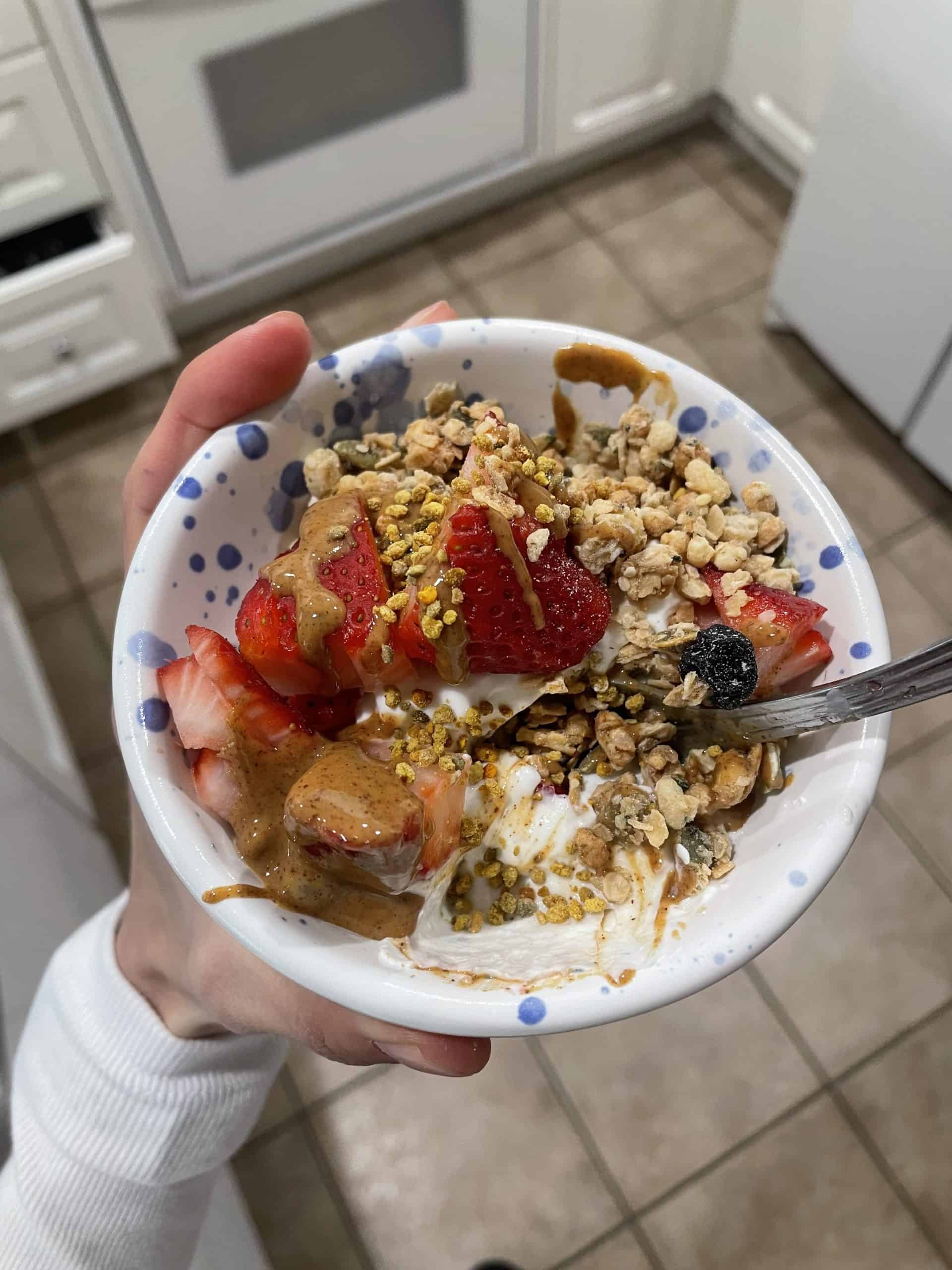 greek yogurt with strawberries, granola and nut butter in a white ceramic bowl with blue polka dots